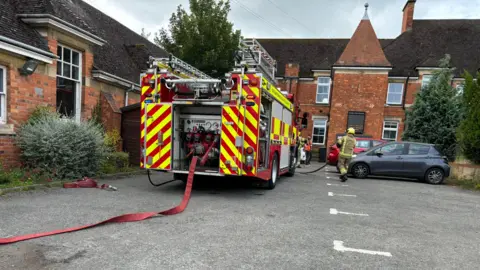 Brick library building with fire engine outside. A long red hose is visible in the foreground