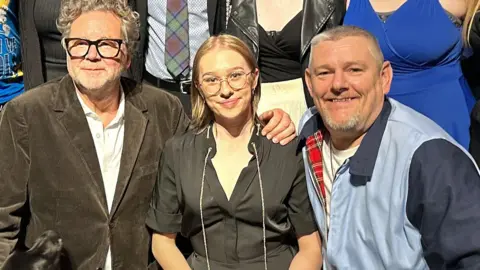 Corey Farwell A woman sat in between two men, all smiling