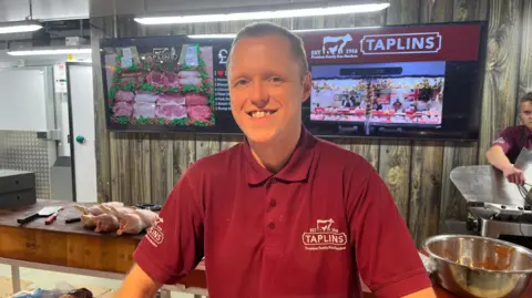 Man wearing Taplins shirt with butchers behind him.