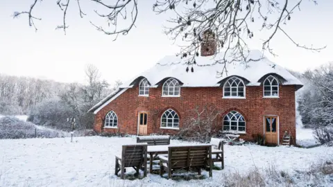 Keith Brooke A cottage pictured on a snowy day. Snow can be seen on its roof, in the garden and in the surrounding fields and trees.
