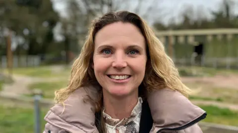 A woman in a brown coat stands in front of the Giraffe enclosure at Paignton Zoo