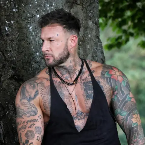 Captureyephotography/Kirk Richards Luke is pictured posing with his tattoos in front of a tree