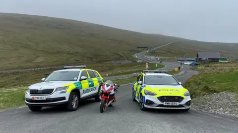 BBC Ambulance, motorbike and police car parked on the Mountain Road by the Bungalow