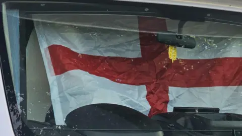 Family An England flag - a red cross on a white background - is covering the windscreen of the campervan.