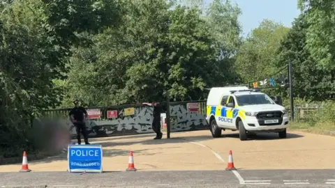 Police car and cones outside lake entrance.