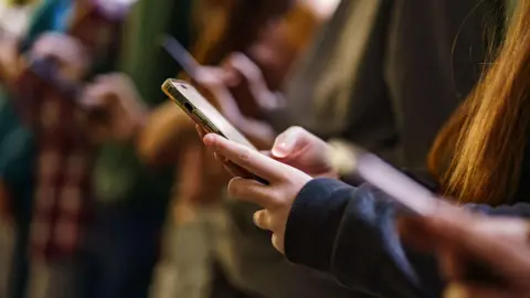 Getty Images A group of young people looking at their smartphones.