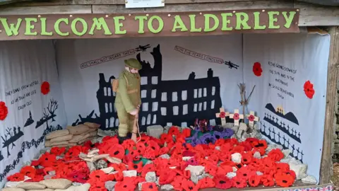 Jane Rhys/Jane Newman Knitted display in Alderley of a remembrance scene with lots of knitted poppies surrounding a soldier.