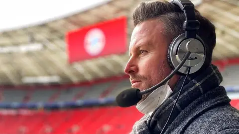 A side profile picture of a man wearing large over the ear headphones with a microphone attached to the side.