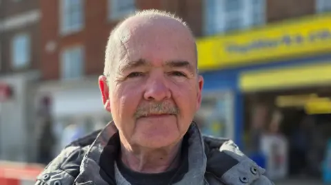 Paul Moseley/BBC Gary Cooper is standing in front of a shop in Great Yarmouth. He's wearing a grey and black coat.