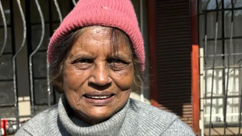 A head and shoulder's shot of a woman wearing a grey jumper and pink beanie hat.