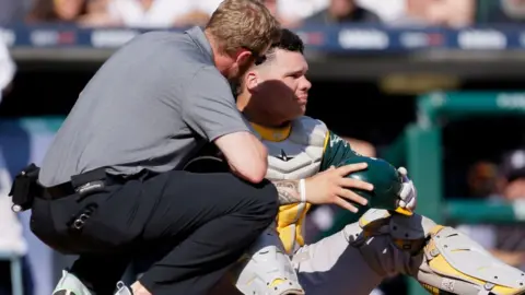 Getty Images Bruce Maxwell is attended to by a trainer after getting hit with a ball on 20 September
