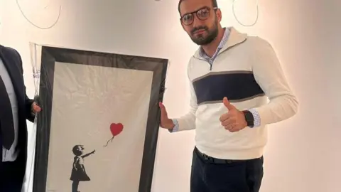 Nick Johnson/BBC News Lindor Mehmetaj holding the recovered artwork giving a thumb up to the camera
