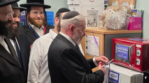 Mid and South Essex NHS Foundation Trust Jewish community and charity leaders cutting a purple ribbon in front of a kosher microwave and freezer.