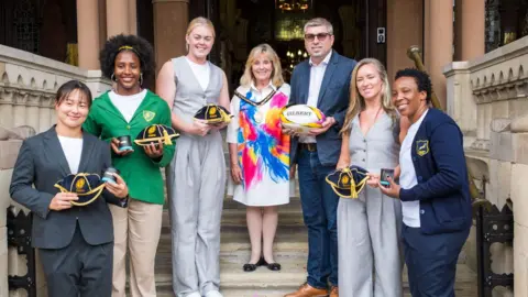 West Northamptonshire Council A group of people including rugby players and local council figures stand on the steps of Northampton's Guildhall building. 