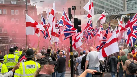 Police can be seen to the side of a group of flag-carrying Britain First supporters. They are carrying Union flags and the cross of St George. 
