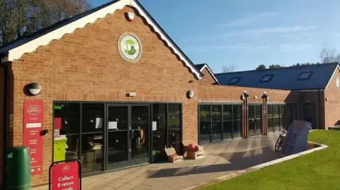 A Google street view screenshot of the outside of the shop. It's a single-storey brick building with big glass doors, and a lawn in front of it.