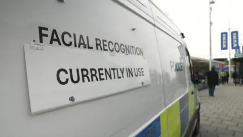Ian Palmer / BBC A police van parked outside a shopping centre. A sign on the van reads 'Facial recognition currently in use'.