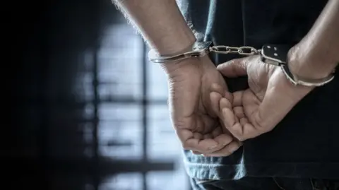 Getty Images Close up of an arrested person with handcuffed hands behind their back.