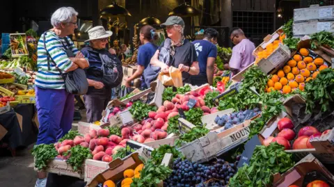 Getty Images Three women buying fresh fruit and vegetables from a market stall in Borough Market, London.