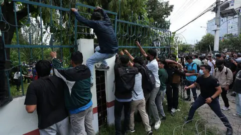 Getty Images A group of ten men stood at a wall as one makes his ascent over the railings outside the parliament building in Kathmandu