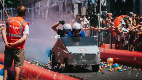 A silver Cybertruck running through colourful smoke