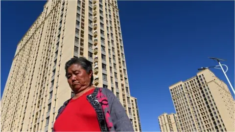 Getty Images A woman walks in front of a housing complex by Chinese property developer Evergrande in Beijing