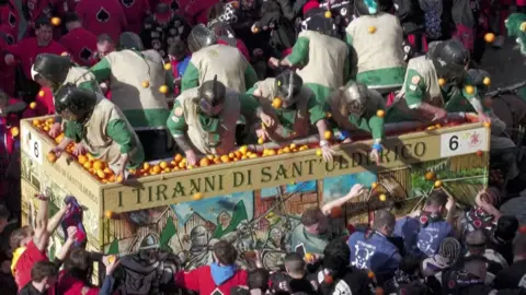 People in car full of oranges throw them at the crowd