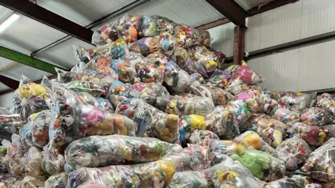 A huge pile of clear plastic bags filled with colourful toys in a warehouse