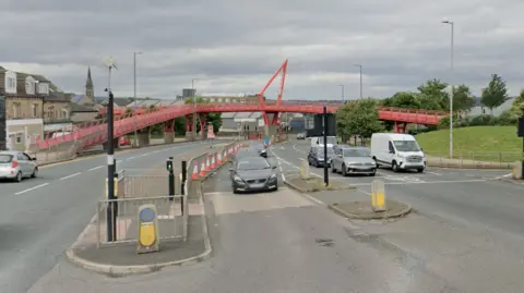 A red metal bridge over a multi-lane road where traffic sits at traffic lights.