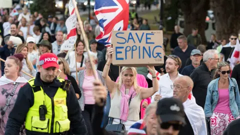 Getty Images Protesters march down a street, some are women wearing pink clothes, one holds a homemade banner reading "Save Epping".