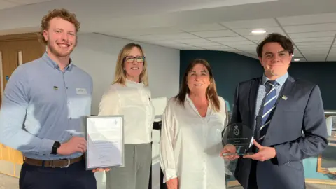 Jon Wright/BBC Four people stand in a line holding an award and a certificate.