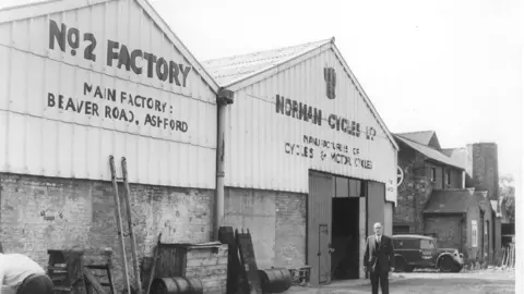 Dover Transport Museum A man in a suit stood outside an industrial building in a black and white image. The signage on the building reads "No 2 Factory Norman Cycles Ltd".