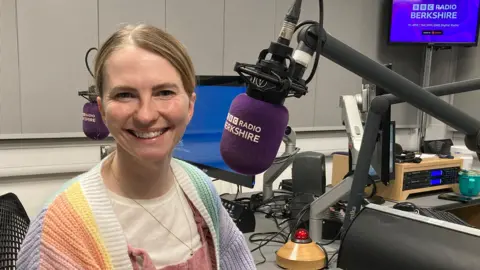 Erin Kennedy is smiling and sitting in front of microphone in the BBC Radio Berkshire studio. 