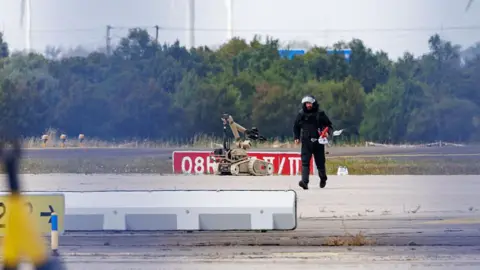 A police investigator works on the tarmac at Leipzig/Halle Airport on August 5, 2026, with a robot next to him