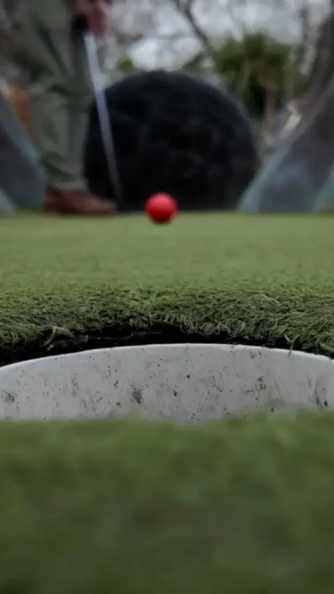 A red gold ball travelling towards a hole on the course.