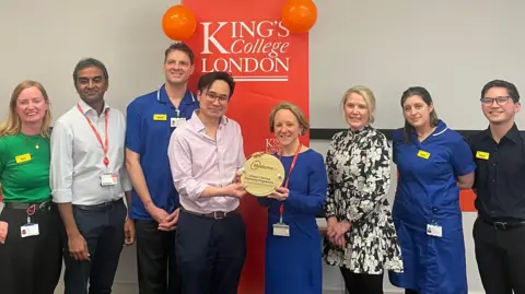 PA Media Eight people from King's College Hospital NHS Foundation Trust stand in a row and hold an award.