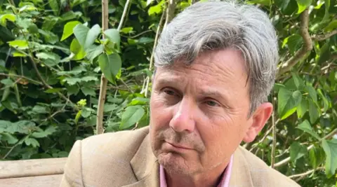 A man with grey hair and a brown suit jacket. 