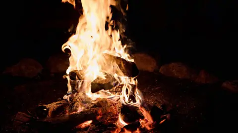 Flames from a wood burning bonfire against a black night sky in the evening.