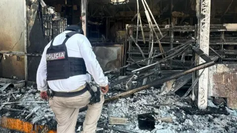 A police officer walking through the rubble of a burnt out building