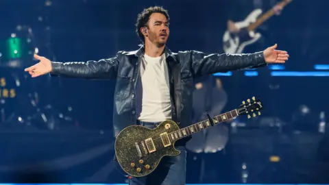 Getty  Kevin Jonas standing on stage, with his arms outstretched.