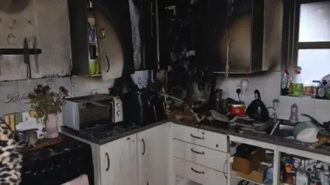 A kitchen after a fire, with blackened cupboards. 