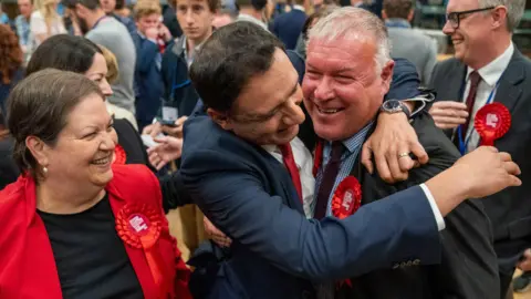 PA Media Davy Russell being hugged by Anas Sarwar as Jackie Baillie looks on.