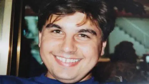 Kam Miller A close up photo of Neil Miller. He has black short hair and is smiling. 