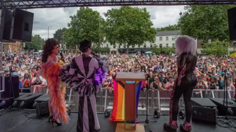 Richard Ashton Performers wearing colourful clothes on stage in Sneinton. A large crowd is in attendance.