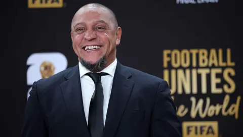 Roberto Carlos smiles for a photo while wearing a suit at the Fifa World Cup draw