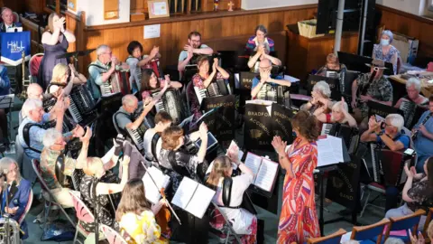 BRADFORD ACCORDION BAND An orchestra with players holding their hands in the air and clapping