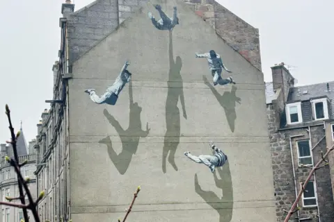 Art work on a building wall showing four people and their shadows.
