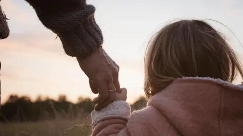 BBC A young girl holding an adult's hand, looking over a field