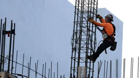 O trabalhador da construção civil ajuda a criar uma coluna auxiliar usando vergalhão de aço durante um edifício da torre. 