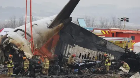 Firefighters conduct search operations at the wreckage site of the Jeju Air aircraft at Muan International Airport in Muan, South Korea, 30 December 2024